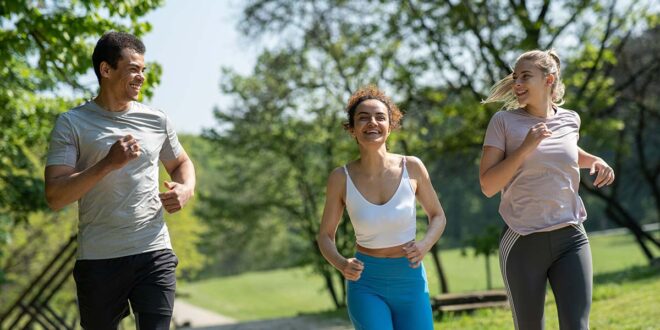 Trójka uśmiechniętych biegaczy trenuje wspólnie w parku w słoneczny dzień